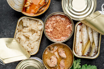 Assortment of canned food cans with different types of fish Salmon, tuna, mackerel and sprats and seafood on a stone background with copy space for your text