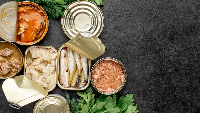Assortment of canned food cans with different types of fish Salmon, tuna, mackerel and sprats and seafood on a stone background with copy space for your text

