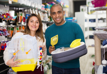 Positive couple choosing bird cage and cat accessories at pet store