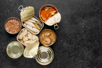 Assortment of canned food cans with different types of fish Salmon, tuna, mackerel and sprats and seafood on a stone background with copy space for your text