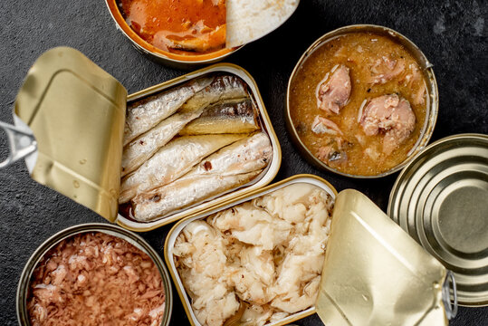Assortment of canned food cans with different types of fish Salmon, tuna, mackerel and sprats and seafood on a stone background 