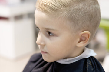 Close-up of boy with new hairstyle at barber shop.