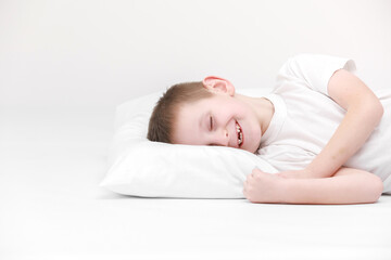 portrait of a happy cute little boy waking up in the morning and lying on a white pillow isolated on a white background. fresh and cozy bedding sheets. Bedtime for kids. concept of happy dreaming