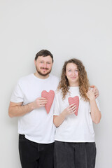 valentines day. young smily man and woman in white t-shirts with red hearts in their hands. couple in love on a white background