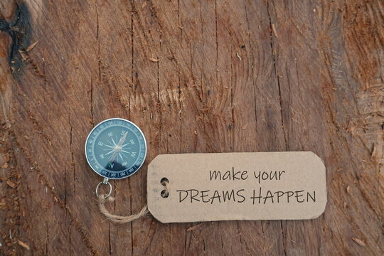 Conceptual Image: Magnetic compass with paper tag written Make Your Dreams Happen at outdoor, selective focus.