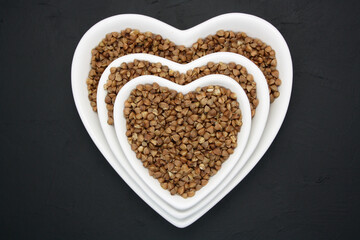 Buckwheat in a heart-shaped bowl on a black background.