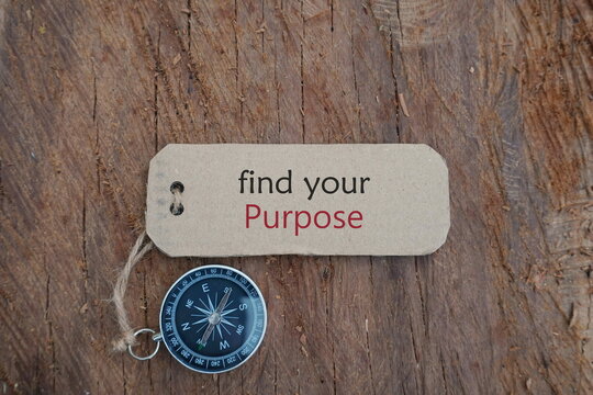 Conceptual Image: Magnetic compass with paper tag written "Find Your Purpose" at outdoor, selective focus.