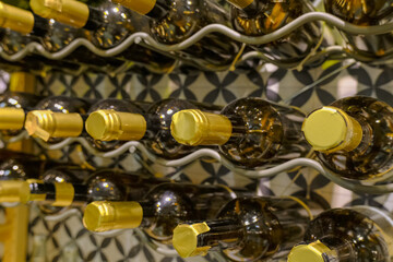 Wine bottles with yellow packaging on metal wine shelves across the wall close-up. Wine production. Wine store.