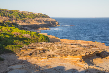 Rocky, cliff seafront coastline and heathland in the Royal National Park on a sunny summer day in...