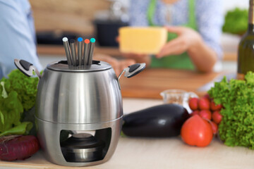 Fondue in a pot at the background of friends cooking together, close-up. Kitchen interiors and cookware