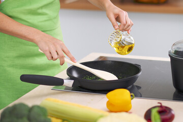 Young woman housewife cooking in the kitchen while adding olive oil. Concept of fresh and healthy meal at home