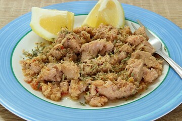 Tuna fish with oregano, olive oil and lemon in a plate and a fork. Closeup, selective focus
