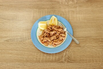 Spicy tuna fish with olive oil and lemon in a plate and a fork, isolated on a wooden table. Top view, selective focus