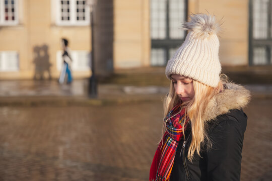 A young blonde female Caucasian tourist visiting the Amalienborg Palace, residence of the Danish Royal Family in Copenhagen with shadows of Royal Life Guards in the background.