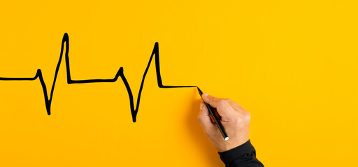 Male hand drawing a electrocardiogram heart beat chart on yellow background. Heart health care and...