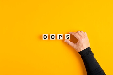 Male hand placing the wooden cubes with the word oops