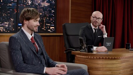 Late-night talk show host having a funny conversation with celebrity male guest in a studio. TV broadcast style show