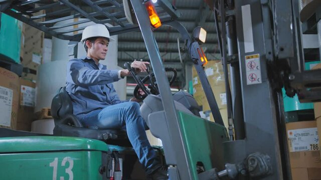professional asian male engineer control fork lift truck loading product pallet with concentrate in warehouse factory distribution infrastructure ideas concept
