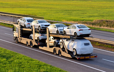 Car carrier trailer transports cars on highway on sunset background. Auto transport and car...