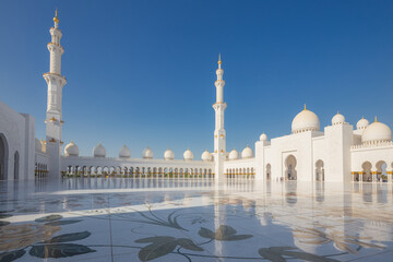 An empty courtyard with and exterior view of the Sheikh Zayed Grand Mosque on a clear sunny day in Abu Dhabi, UAE.