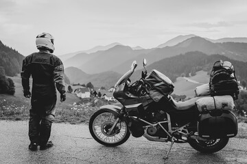 Obraz na płótnie Canvas Back view motorcycle driver with motorbike, Adventure vacation, biker dressed in raincoat. sealed bag, water resistant, overalls. Mountains road trip, side bags equipment. copy space. Black and white