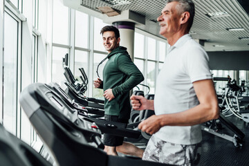 Fototapeta na wymiar Two people on the treadmill, in the focus of a handsome young coach, he is smiling at the camera. Sports, gym, healthy lifestyle