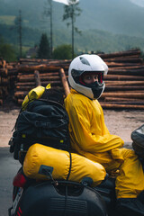 A girl in a raincoat, shoe covers and a helmet is sitting on big adventure motorbike. Vacation and...