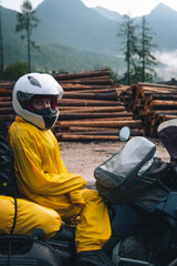 A girl in a raincoat, shoe covers and a helmet is sitting on big adventure motorbike. Vacation and...
