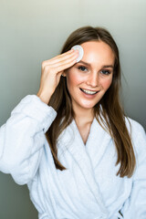 Fototapeta premium Beautiful woman touching her face with sponge and smiling while standing in front of the mirror