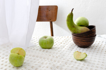 Fresh juicy apples and pear on the tablecloth, wooden rustic chair, white curtains.Concept of countryside and summer