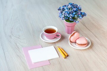 A cup of tea with heart shaped macarons, bouquet of forget-me-not flowers and card for congratulation text on a table. Holiday background, copy space, soft focus, top view