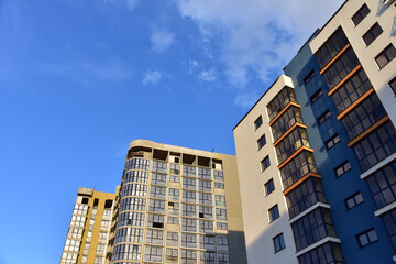 Fototapeta premium Facade of a new modern high-rise residential building. Skyscraper on blue sky background. Tall house renovation project, government programs. Minimalistic multi storied home.