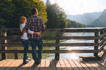 Back view of lovely couple Posing. On the background a beautiful sunset on the lake. Rest and vacation in nature. Wooden pier. Bohinjsko jezero Slovenia