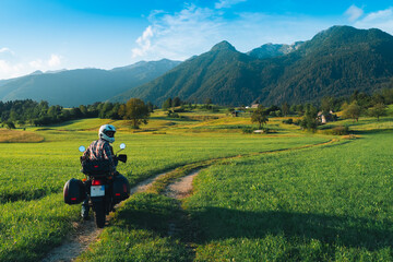 Fototapeta na wymiar Man motorcyclist ride touring motorcycle. Alpine mountains on background. Biker lifestyle, world traveler. Summer sunny sunset day. Green hills. hermetic packaging bags. copy space. Slovenia