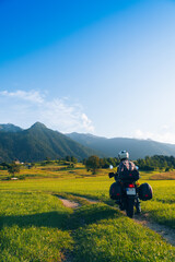 Man motorcyclist ride touring motorcycle. Alpine mountains on background. Biker lifestyle, world traveler. Summer sunny sunset day. Green hills. hermetic packaging bags. Vertical photo. Slovenia