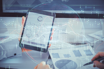 Double exposure of man's hands holding and using a digital device and forex graph drawing. Financial market concept.