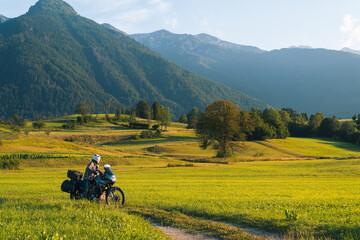 Man motorcyclist ride touring motorcycle. Alpine mountains on background. Biker lifestyle, world traveler. Summer sunny sunset day. Green hills. hermetic packaging bags. copy space. Slovenia