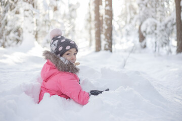 Fototapeta na wymiar Cute girl playing outdoor in winter fresh white snow sitting on ground.