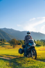 Obraz premium Man motorcyclist ride touring motorcycle in action. Alpine mountains on background. Biker lifestyle, world traveler. Summer sunny sunset day. hermetic packaging bags. Vertical photo. Slovenia
