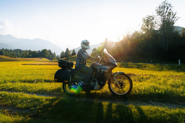 Fototapeta na wymiar Man motorcyclist ride touring motorcycle. Alpine mountains on background. Biker lifestyle, world traveler. Summer sunny sunset day. Green hills. hermetic packaging bags. Slovenia