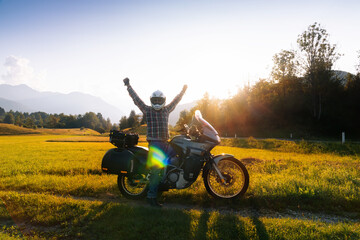 Fototapeta na wymiar Man motorcyclist happy destination scene. Motorcycle adventure. Alpine mountains on background. Biker lifestyle, world traveler. Summer sunny sunset day. copy space. Slovenia