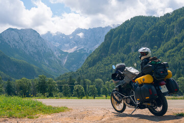 Girl in full body protection, turtle armor, knee pads and helmet, tourer motorcycle for traveling with large luggage, on a background of green mountains, travel and freedom. Zgornje Jezersko Slovenia