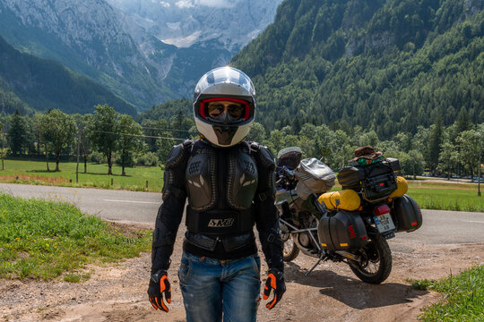 Portait, woman in full body protection, turtle armor, knee pads and helmet, tourer motorcycle for traveling on a background. Green mountains, travel and freedom. Zgornje Jezersko Slovenia