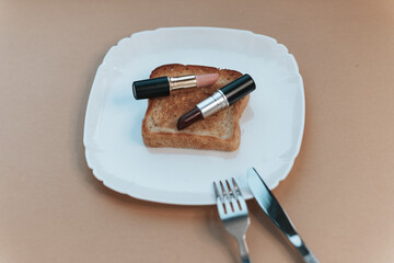 Makeup artist breakfast. 2 lipsticks on toast on a white plate with a fork and knife.