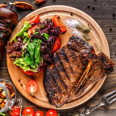 Beef T-Bone steak, herbs and spices on a dark table. Top view. Free space for your text.