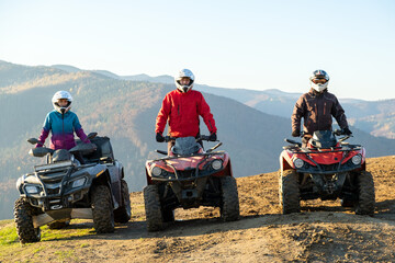 Happy drivers in protective helmets enjoying extreme ride on ATV quad motorbikes in fall mountains at sunset. © bilanol