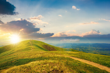 mountain landscape on a bright spring sunset. path through meadow in grass on the hill in evening light. wonderful weather with fluffy clouds on the sky. borzhava ridge of carpathians