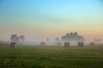 haystack on green field under the beautiful blue cloudy sky at  sunrise. foggy morning. summer (spring) landscape