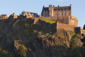 The iconic Edinburgh Castle in golden light perched atop Castlehill on a summer evening as seen from Princes Street Gardens, Scotland.