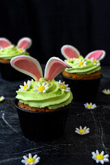 Easter cupcake with whipped green cream. Bunny ears stick out and daisies. low key